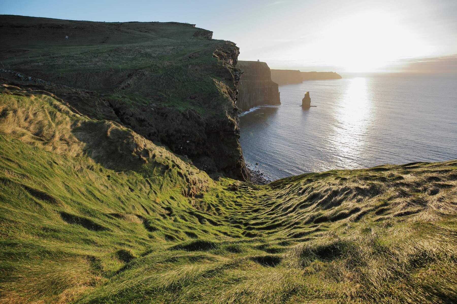 A breathtaking photo of the iconic Cliffs of Moher in County Clare, Ireland, with the rugged cliff face stretching 702 feet above the crashing Atlantic Ocean waves below, set against a dramatic sky.