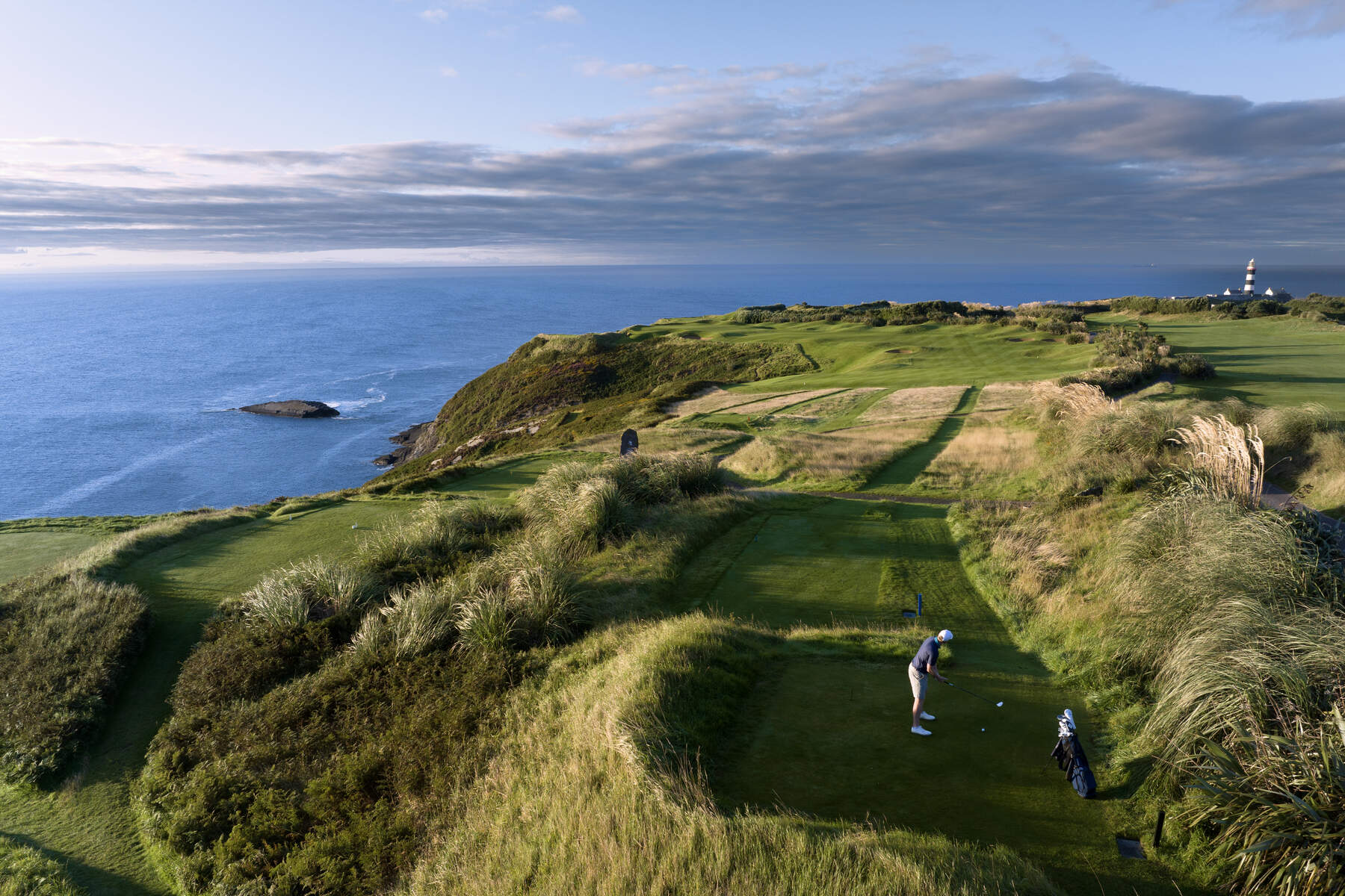 A scenic view of the 2nd hole, known as the 'Gun Hole', at Old Head Golf Links in Kinsale, County Cork, Ireland, featuring a challenging tee shot over rugged cliffs and the Atlantic Ocean, with the historic Old Head Lighthouse in the distance. 