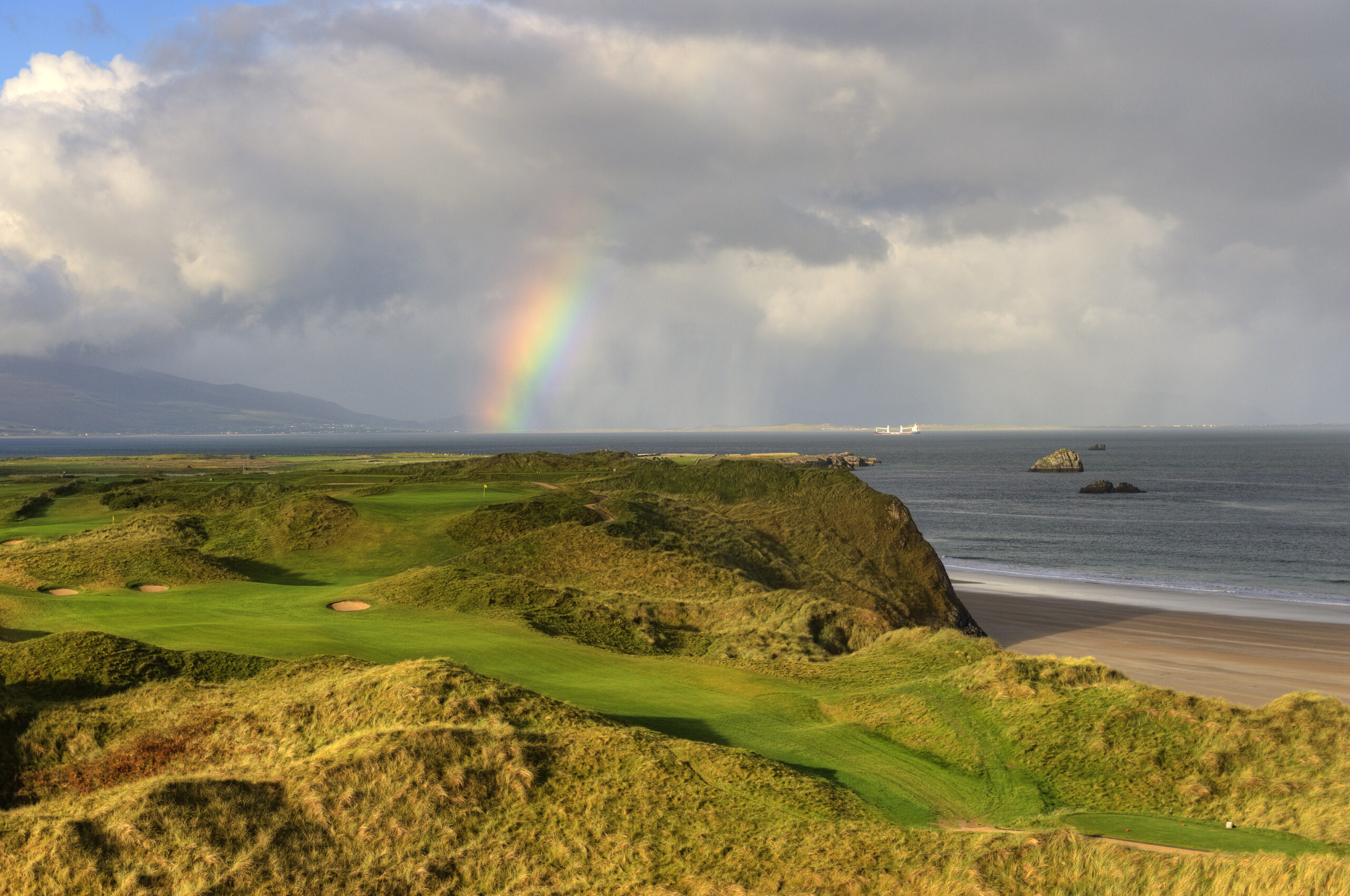 Aerial view of Tralee Golf Course: lush fairways, rugged coastal cliffs, and Atlantic Ocean views.