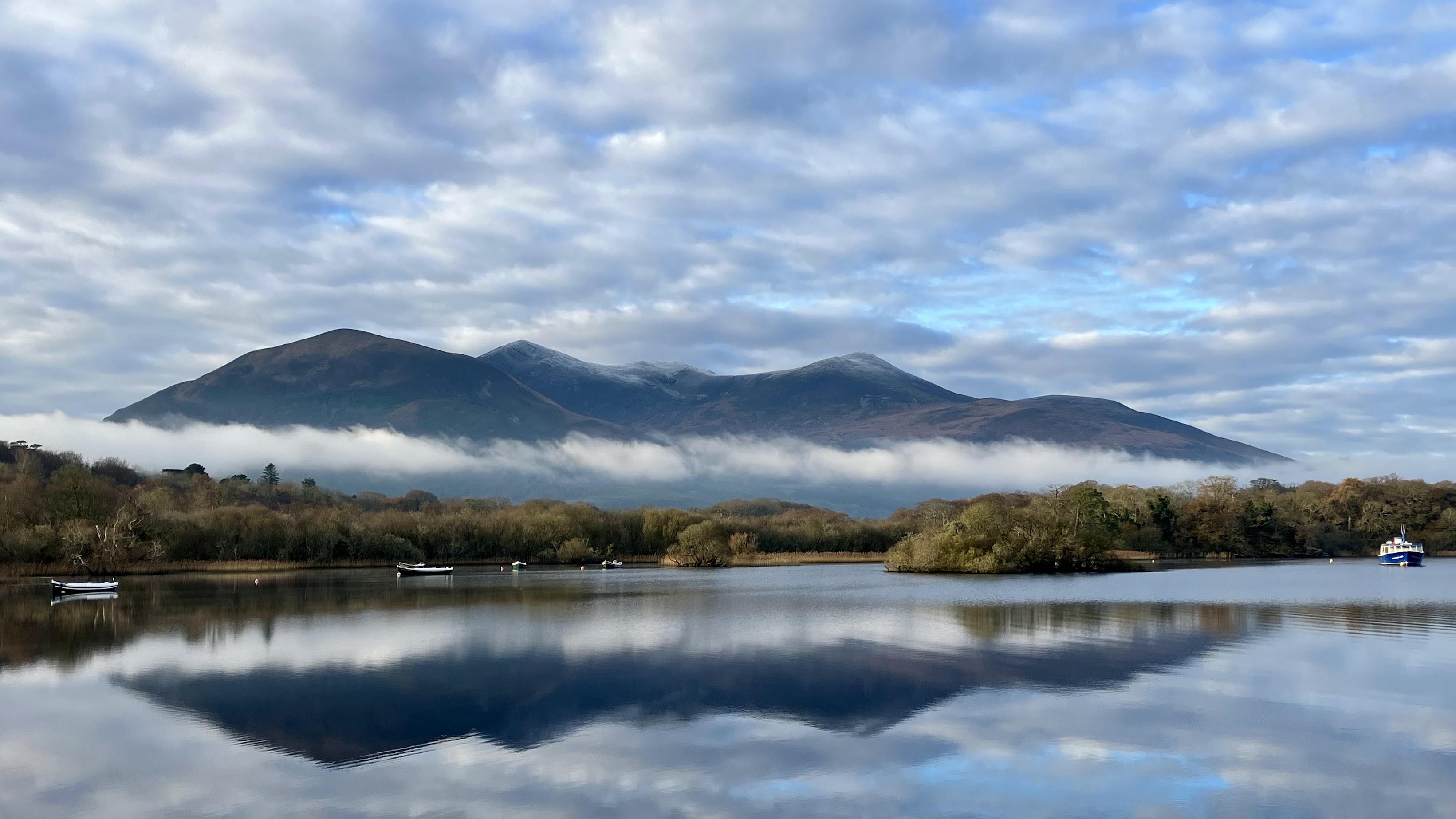 A breathtaking photo of the view from Ross Castle in Killarney National Park, County Kerry, Ireland, showcasing the serene lakes, lush greenery, and majestic mountains of the park. 