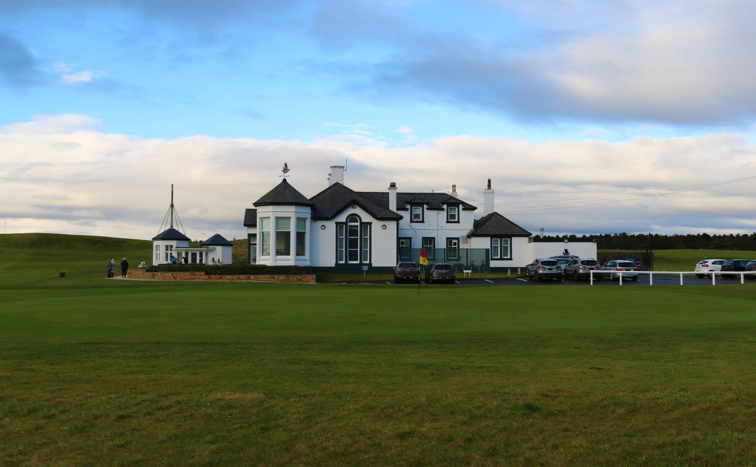 An elegant view of the historic Elie Golf House, nestled on the scenic Fife coast. The charming clubhouse, with its classic architecture, overlooks the lush green fairways and the stunning coastal landscape, offering a unique and picturesque golfing experience.