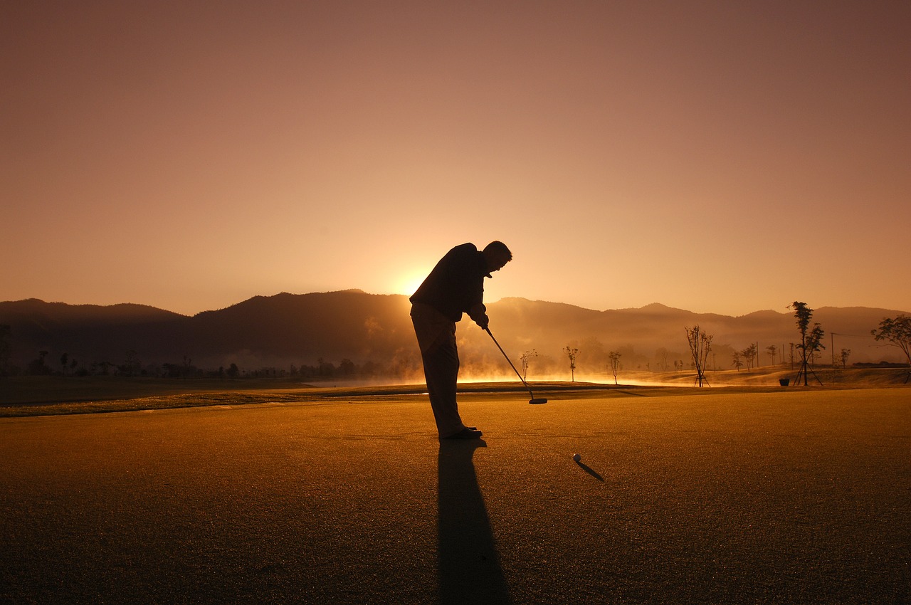 A silhouette of a man golfing at sunset