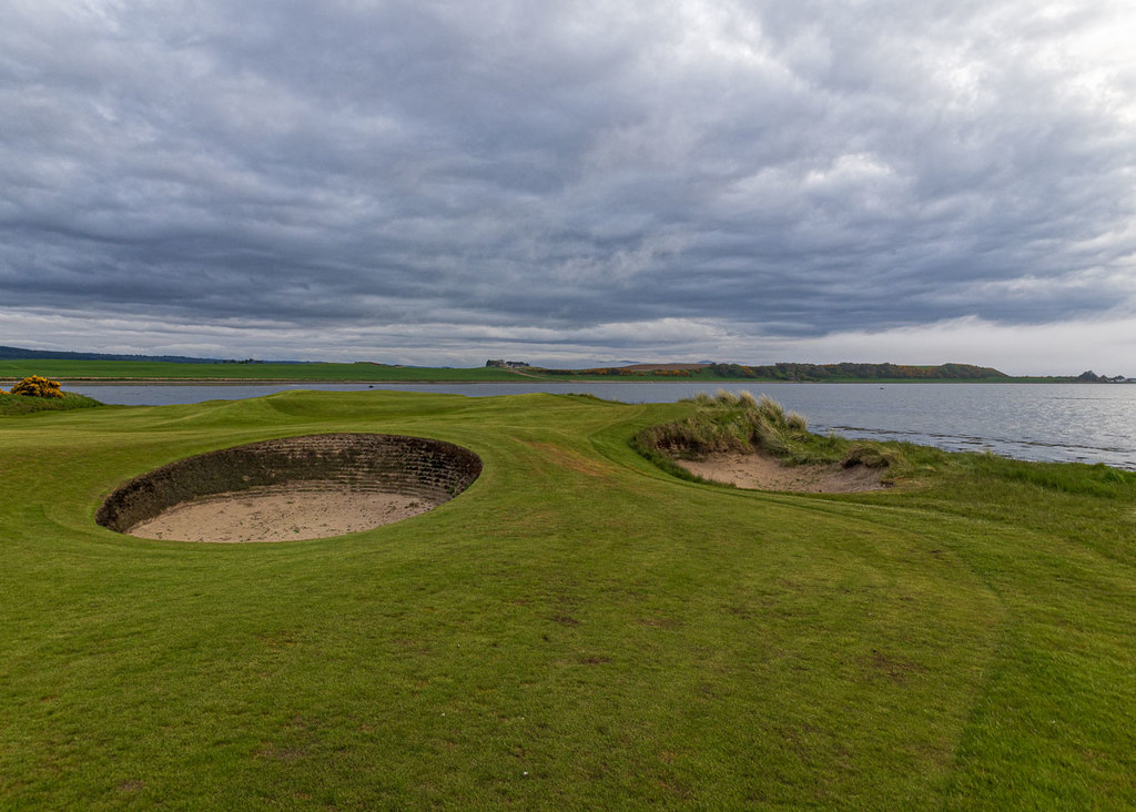 A view of a hole on Castle Stuart Golf Links (Cabot Highlands) with a sand trap in the foreground and water in the background.